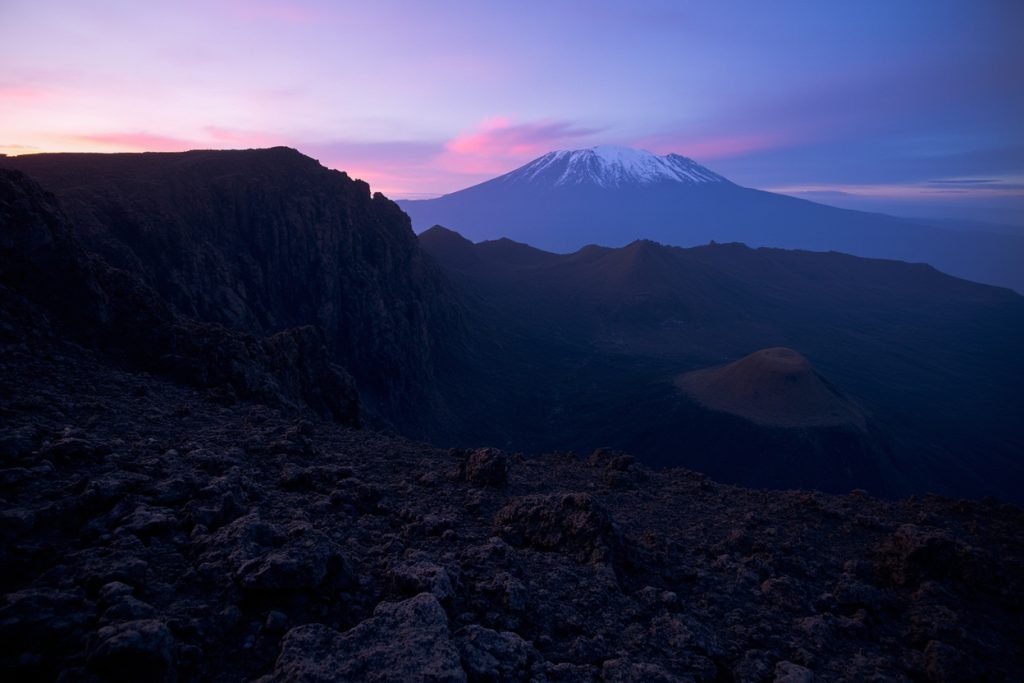 Mount Meru's volcanic crater rim at twilight with distant Kilimanjaro silhouette, Tanzania.