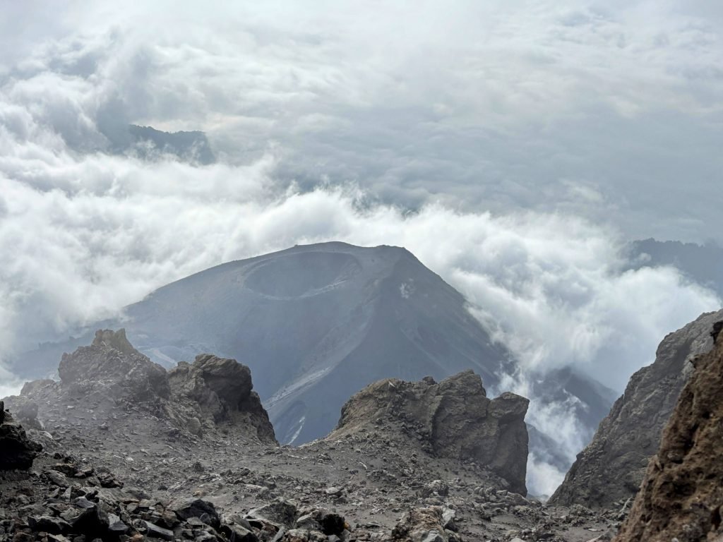 View into Mount Meru's volcanic crater from the summit, ash cone surrounded by clouds, Tanzania.